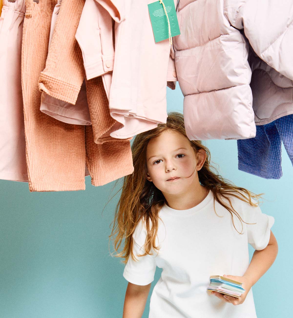 Young girl standing under hanging children's clothing with a blue background